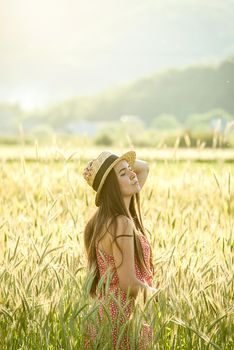 young woman in straw hat in the middle of wheat field enjoing summertime