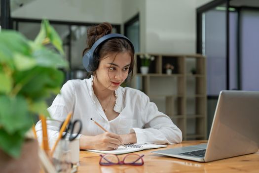Happy young asian girl with wireless headphones looking at laptop screen, reading listening online courses, studying remotely from home due to pandemic corona virus world outbreak, quarantine time