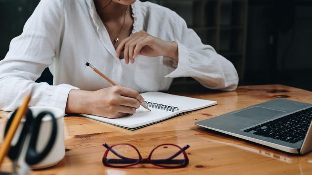 Cropped photo of woman writing making list taking notes in notepad working or learning on laptop indoors- educational course or training, seminar, education online concept