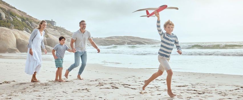 Happy caucasian parents and kids playing with a toy plane while enjoying quality time on a relaxing fun family summer vacation together at the beach. Loving mom and dad bonding with cheerful sons.