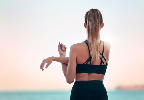 Rearview beautiful woman practising yoga exercise on the beach. Young female athlete stretching and warming up while working out outside. Finding inner peace and balance. Health and lifestyle.