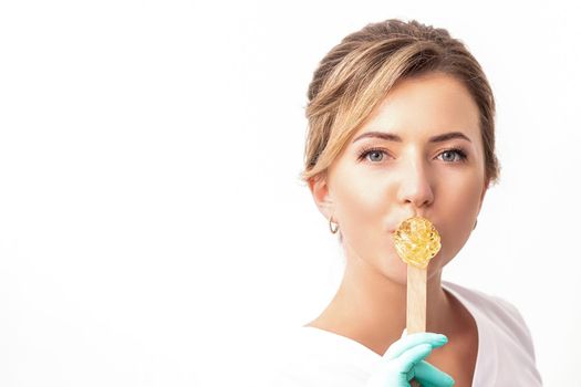 Portrait of female cosmetologist holds a wooden stick with a wax covering her lips on white background