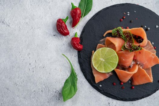 Fresh salmon slices with peppers, greens and lime on concrete background