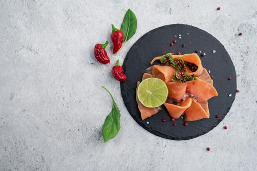 Fresh salmon slices with peppers, greens and lime on concrete background