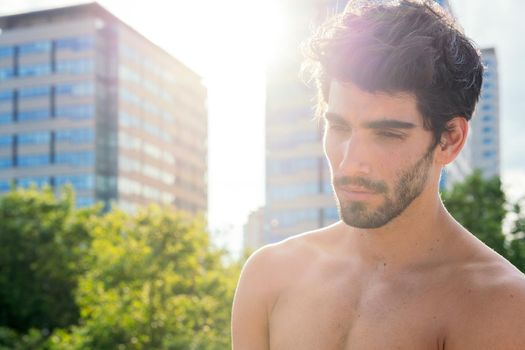 portrait of a handsome shirtless sportsman posing at sunset in front of city buildings, concept of urban sport and healthy lifestyle, copy space for text