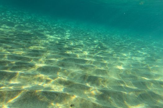 Sea bottom near sandy beach, sun lights on sand "dunes". Underwater photo, abstract marine background.