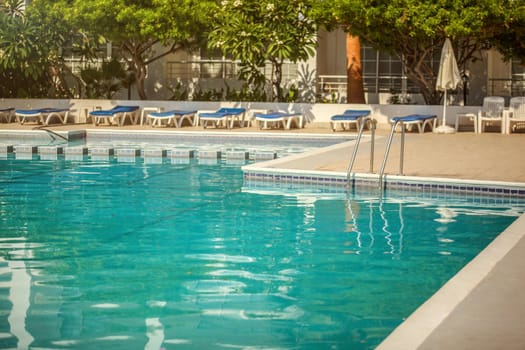 Empty hotel resort swimming pool, lit by morning sun, few leaves on the water surface