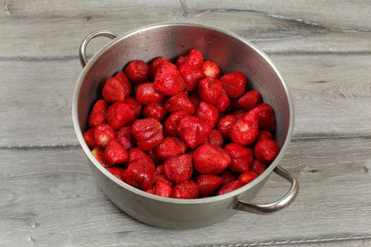 Stainless steel cooking pot full of strawberries on wooden desk. Homemade strawberry jam preparation.