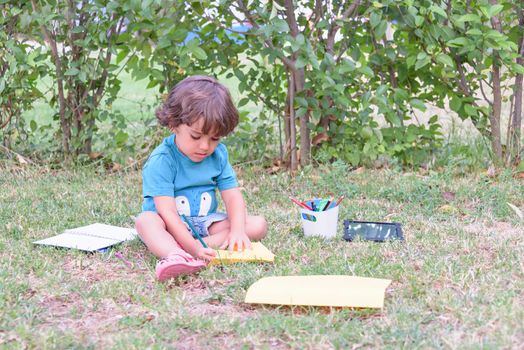 Little boy are using a magic pen to draw pictures in a book on a wooden table in park With face expression of determination