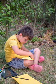 Kid draws in park laying in grass having fun on nature background