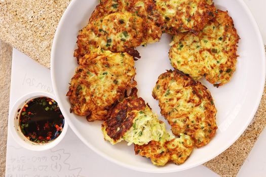 Zucchini fritters, vegetarian zucchini fritters on a white plate served with soy sauce in a small white bowl. Vegetarian food