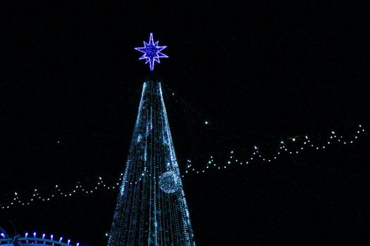 Artificial Christmas tree with garlands, a star and other types of illumination. Christmas concert. Christmas tree at night.