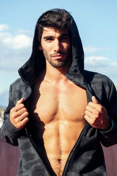 handsome sporty man showing off his muscles under a hooded sweatshirt, concept of sport and healthy lifestyle