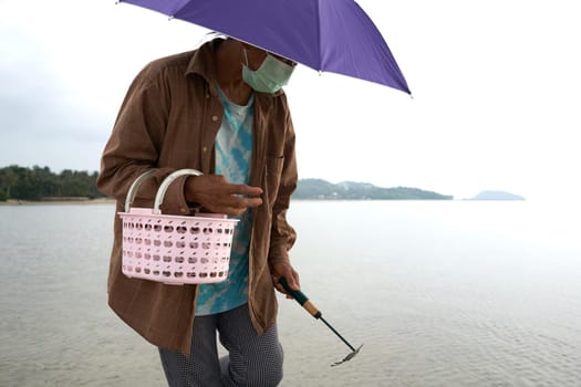 Ko Phangan, Thailand, March 15, 2022: covered and protected aged woman collecting alive clams