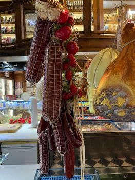 Sticks of sausage, a piece of ham, tomatoes hanging from the ceiling in a supermarket. High quality photo