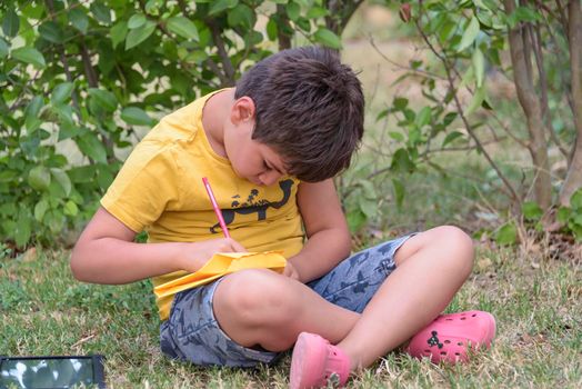 Kid draws in park laying in grass having fun on nature background