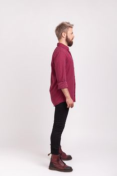 Side view full body length of serious confident bearded male wearing red plaid shirt and casual black pants posing, practicing modeling. Indoor studio shot isolated on gray background