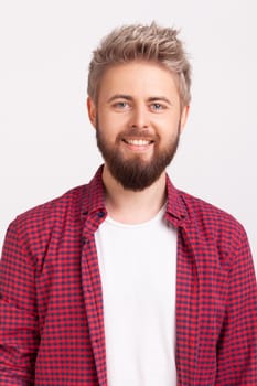 Portrait of cheerful bearded young adult male in plaid shirt sincerely smiling looking at camera, optimistic lifestyle. Indoor studio shot isolated on gray background