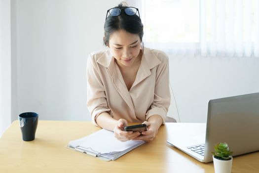 new normal, a businesswoman using mobile phone and computer to work for a company Via the internet on your desk at home.