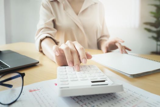 Business woman using calculator to review balance sheet annual using document and laptop computer to calculating budget. audit and Check integrity before investment concept