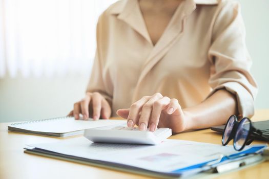 Business woman using calculator to review balance sheet annual using document and laptop computer to calculating budget. audit and Check integrity before investment concept