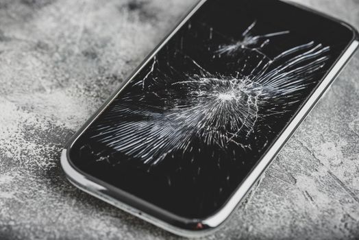 Smartphone with cracked screen over concrete background