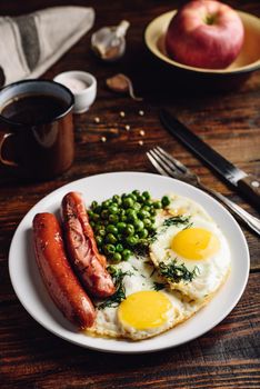 Breakfast with fried eggs, sausages and green peas on white plate