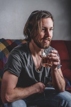 Bearded man listening to music with headphones and holding glass with tea in his hand