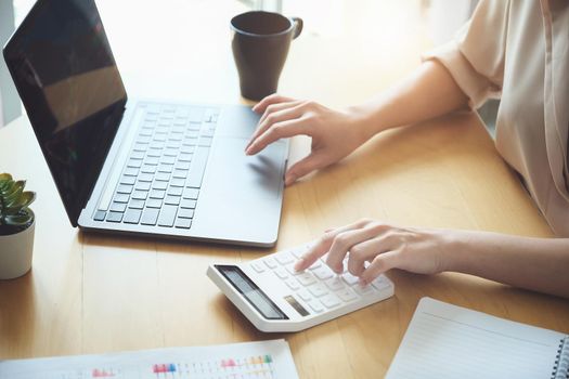 Business woman using calculator to review balance sheet annual using document and laptop computer to calculating budget. audit and Check integrity before investment concept.