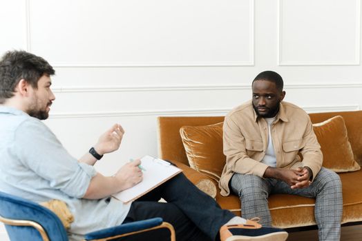 A black male patient undergoing a psychotherapy session with a counselor at a mental health clinic. Young man with emotional problems consults professional therapist.