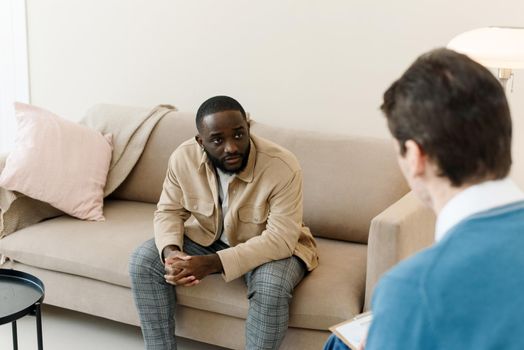 Unhappy young black man having session with professional psychologist at mental health clinic. Professional psychological help concept