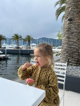 Little girl eating ice cream with a spoon at the table. High quality photo