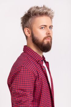 Side view portrait of handsome concentrated bearded young adult man in plaid t-shirt thoughtfully looking to side. Indoor studio shot isolated on gray background
