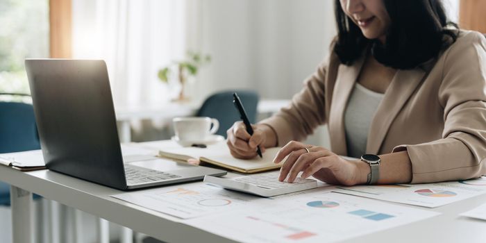 Accountant bookkeeper works on analyzing financial data using a calculator and writing notes with calculations. Accounting Concepts and Personal Financial Planning.