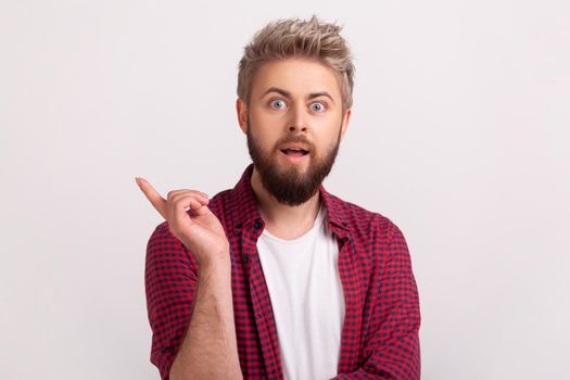 Portrait of inspired bearded man with opened mouth pointing finger up and looking at camera, having good idea, inspiration. Indoor studio shot isolated on gray background