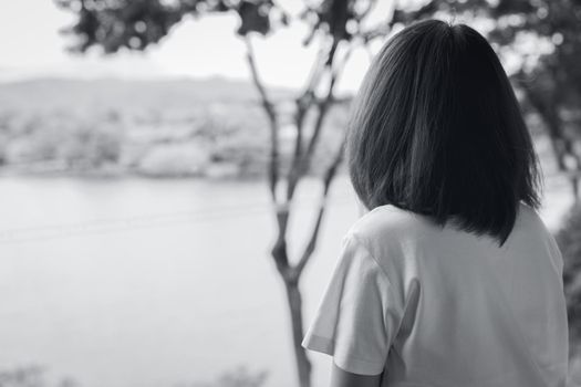 Back view of sad Asian woman in the park look the view of lake. Depressed woman. Mental health concept. Worry and anxiety woman. Unhappy life. Alone and lonely person. Black and white photography.