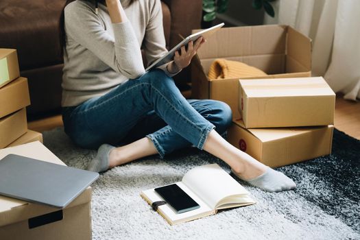 Image of Young asian woman startup freelance with parcel box and talking with customer by tablet. Online marketing packing box delivery concept