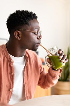 Vertical profile portrait of African American black man drinking healthy green juice with bamboo straw. Wellness and healthy lifestyle concept.