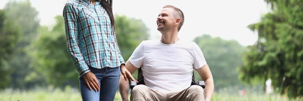 Portrait of man sit in wheelchair, female visitor spend time with friend at nursing house. Happy and smiling middle aged guy. Disability, recovery concept