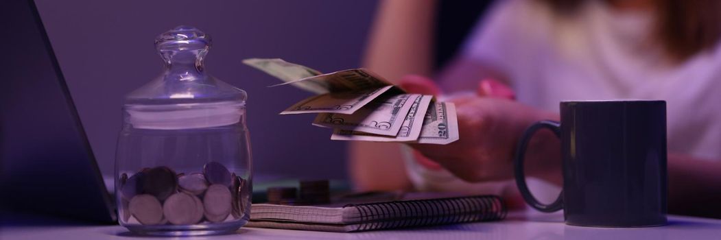 Close-up of broken young woman counting cash money, glass container with coins on desk . Saving up for tomorrow, pay bills. Finance, family budget concept