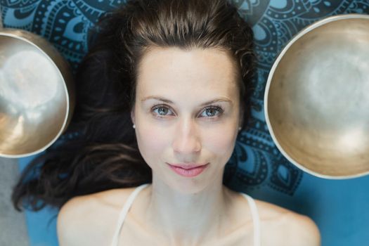 Yoga concept, meditation and sound therapy. Portrait of beautiful young caucasian woman surrounded by copper tibetan singing bowls and instruments.