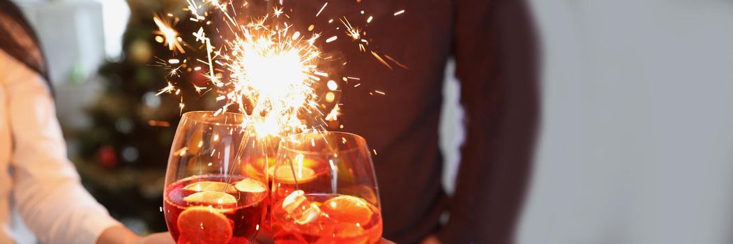 Close-up of people raise fire sparklers and glass filled with champagne and celebrate winter holiday together. Party, nightlife, new year, festive concept