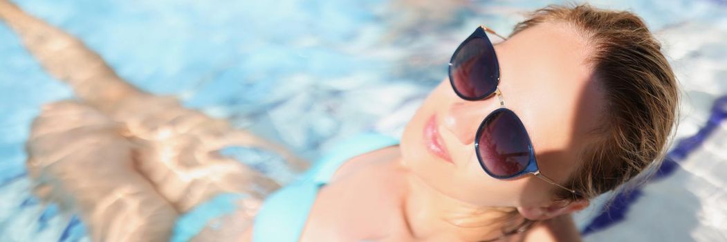 Top view of happy young female sit in pool wearing trendy glasses. Relaxing atmosphere on vacation, sunny day. Holiday, resort, hotel, time alone concept