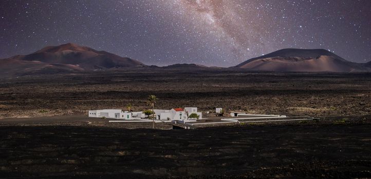 Amazing nocturnal panoramic landscape of volcano craters in Timanfaya national park. Milky way stars on night sky over La Gueria, Lanzarote island, Canary islans, Spain.