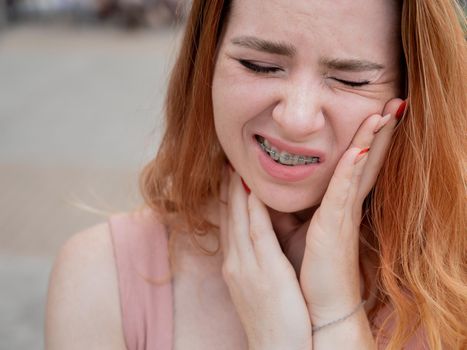 Young red-haired woman with braces suffering from pain