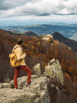 Traveler stands and enjoys the view from hilly viewpoint on cloudy day in autumn. Traveling on hill peaks landscape