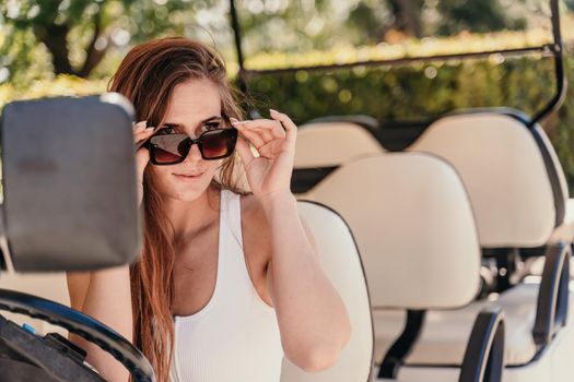 A middle-aged woman is driving a car for transporting tourists. Electric car, Tourist bus. Car for transporting people around the hotel, park, golf club.