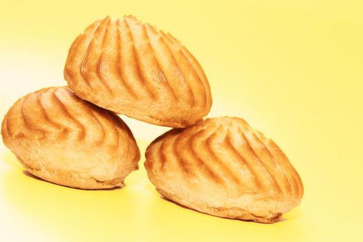 an item of soft, sweet food made from a mixture of flour, shortening, eggs, sugar, and other ingredients. Three delicious appetizing profiterole eclair cakes on yellow background