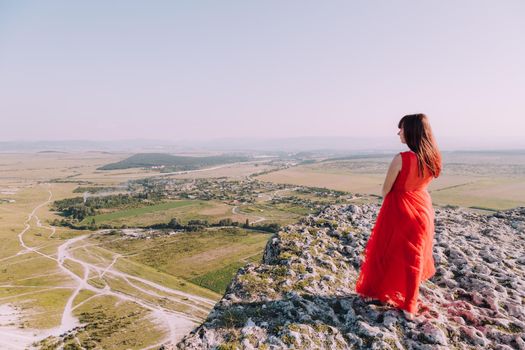 A girl in a red dress on the background of the mountains lifestyle. Illustrating articles about travel. A girl with a beautiful view. Vacation in Crimea. White rock. View of the villages. Lifestyle processing. Copy space .