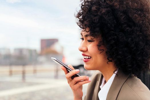young latin woman smiles happy recording a voice message with a mobile phone, concept of communication and urban lifestyle, copy space for text